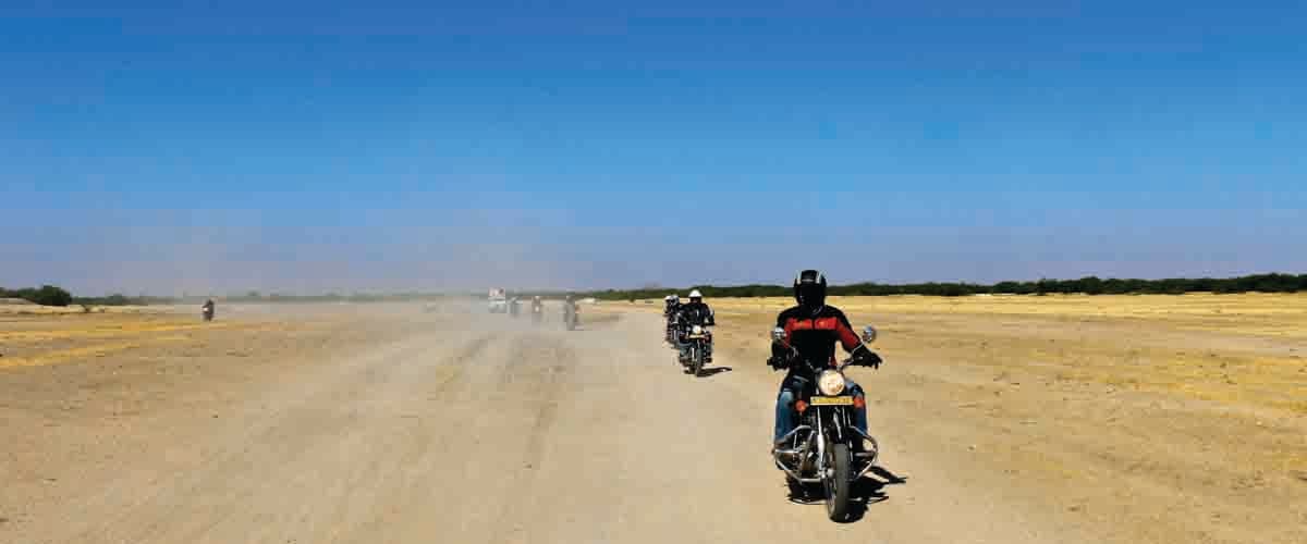 Indian Rides, groupe de voyageurs à moto Royal Enfield traversant un paysage désertique du Rajasthan Indian Rides, groupe de voyageurs à moto Royal Enfield traversant un paysage désertique du Rajasthan